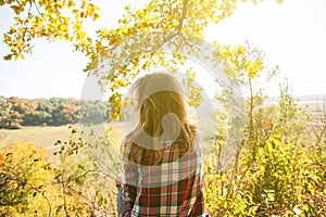 Girl in the checkered shirt is sitting in the autumn forest. Seasonal concept. Stylish hipster clothes outdoors. Nature philosophy