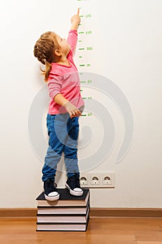 Girl checking height on growth chart at four books