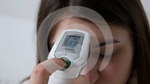 Girl checking temperature with an electronic medical infrared thermometer. Healthcare and medical care concept