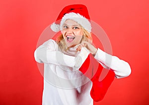 Girl cheerful face check out gift in christmas sock. Woman in santa hat unpacking christmas gift red background. Check