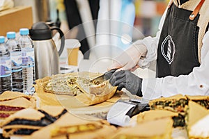 Girl Chef cook in apron and gloves cuts freshly baked pie in market. Street food