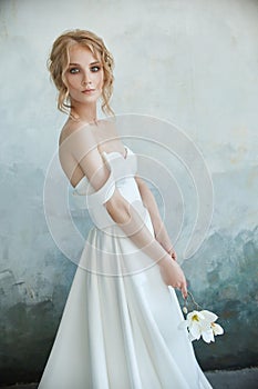 Girl in a chic long dress sitting on the floor. White wedding dress on the bride`s body. Beautiful light dress with a long hem, a