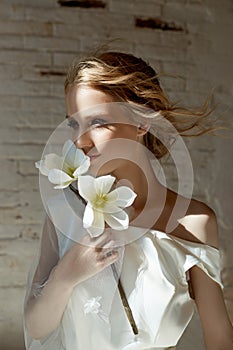 Girl in a chic long dress sitting on the floor. White wedding dress on the bride`s body. Beautiful light dress with a long hem, a