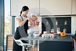 Girl is in the chief hat. Mother with her daughter are preparing food on the kitchen