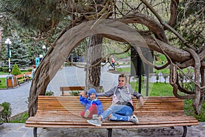 A girl with a child on a bench under the branches of a tree in Borjomi Park, on a rainy day. Georgia 2019