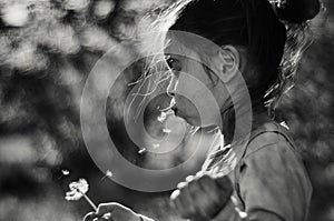 Girl child blowing on a dandelion flying seeds