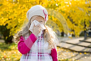 Girl child with cold rhinitis on autumn background, flu season, allergy runny nose