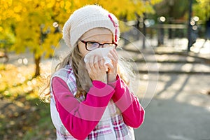 Girl child with cold rhinitis on autumn background, flu season, allergy runny nose