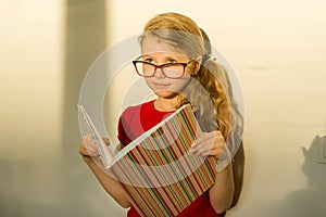 Girl child elementary school student wearing glasses is holding a textbook and dreamily smiling looking forward