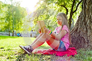 Girl child in glasses reading book in the park