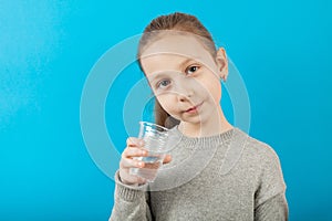 Girl child hold in hand pure mineral water from glass, portrait on blue background