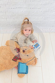 Girl, child measures the pressure of the toy bear, plays doctor