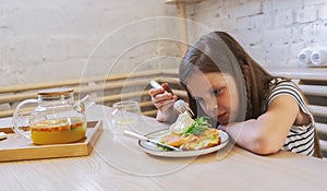 Girl child misses in a cafe and sadly looks at the plate with food.