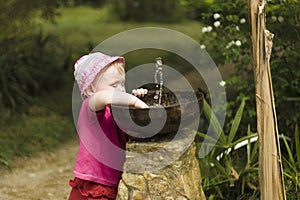 Girl child playing with small fountain bubbler in the park