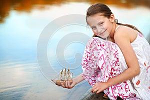 Girl child playing with a toy sailing ship by the river