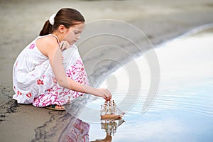 Girl child playing with a toy sailing ship by the river
