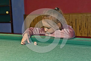 Girl child plays on the billiard table.