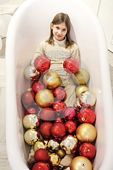 Girl child is posing in bathtub with christmas balls