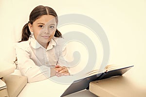 Girl child read book sit table white interior. Schoolgirl studying textbook. Kid school uniform happy face read book