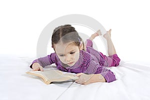 Girl child reading book lying on bed