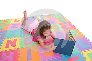 Girl child reading kids book on alphabet mat