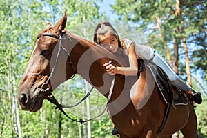 Girl child riding horse, summer horse ride in the forest, girl lovingly hugged horse