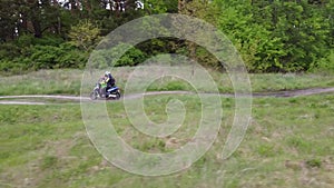 A girl and a child riding a moto scooter or motorcycle along a dirt road between field and forest.Aerial, drone footage.