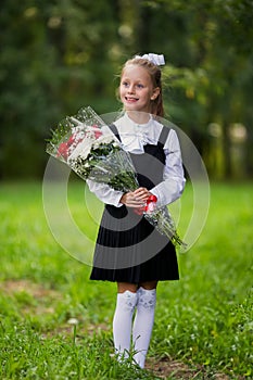 A girl child in school uniform goes to the school on September 1st. The girl is holding a bouquet of flowers. Close-up