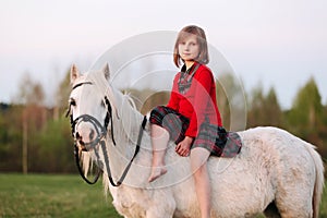 Girl child is sitting on a small white horse looking into the camera