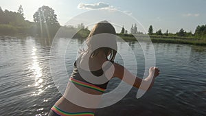 Girl child in a swimsuit jumps from a pier into a pond