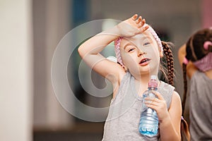 Girl child is tired after training fitness exercises in health club, drink water.