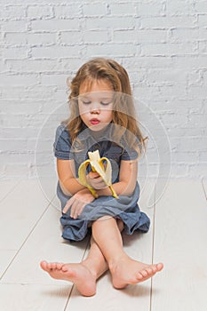 A girl, a child to eat delicious healthy banana against a brick