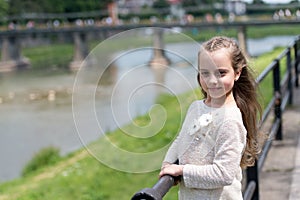 Girl child tourist enjoy sightseeing while walks. Kid girl with long hair walks near riverside, river on background