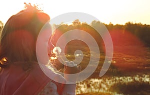 girl child in the twilight light of the setting sun, holding a white fluffy dandelion, glare of sun rays       .
