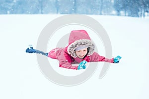 Girl child in warm clothes red pink jacket playing with snow having fun during cold winter snowy