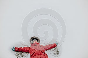 Girl child in warm clothes red pink jacket playing with snow having fun during cold winter snowy