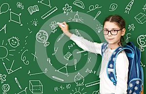 Girl, child writes on a wooden green board, holding white chalk in his hand.