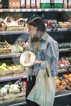 Girl chooses fruits and vegetables in the store with eco bag. Holding a melon and avocado