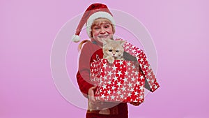 Girl in Christmas red sweater hat smiling, unwrapping gift, opening box with pet cat, great surprise