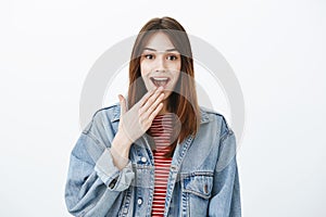 Girl chuckling from amazement. Portrait of pretty young european female student in denim jacket, holding palm near