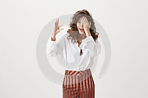 Girl chuckling from surprise and amazement, covering one eye with palm and shaping something little or small with hand