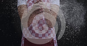 Girl claps hands and spraying flour over dough on dark background.