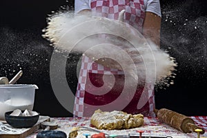 Girl claps hands and spraying flour over dough on dark background. Professional girl baker  is preparing cookies