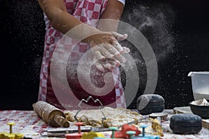 Girl claps hands and spraying flour over dough on dark background. Professional girl baker  is preparing cookies