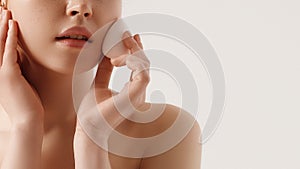 Girl cleaning face with cotton sponge. Beautiful model with shiny clean skin. Isolated on white background