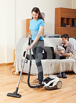Girl cleaning at home while man with cat