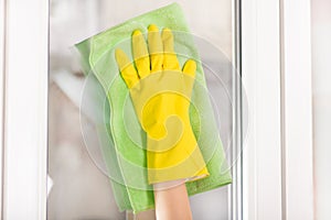 Girl cleaning window at home with green rag and yellow protective glove