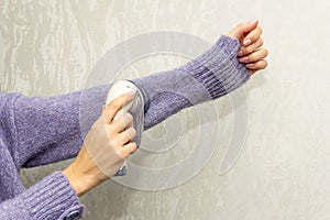 The girl cleans a knitted wool sweater with a electric fabric shaver to remove pellets, small lumps that have piled on the surface