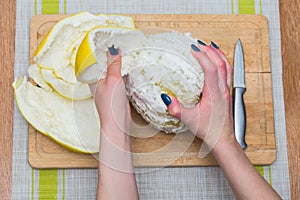 Girl cleans a pomelo on a wooden board