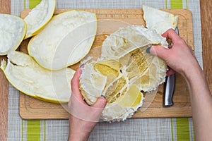 Girl cleans a pomelo on a wooden board